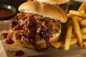 A pulled pork sandwich with lots of BBQ sauce and french fries.